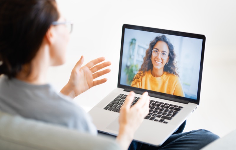 Young woman is using laptop for remote conversation with friend. People having fun staying at home.